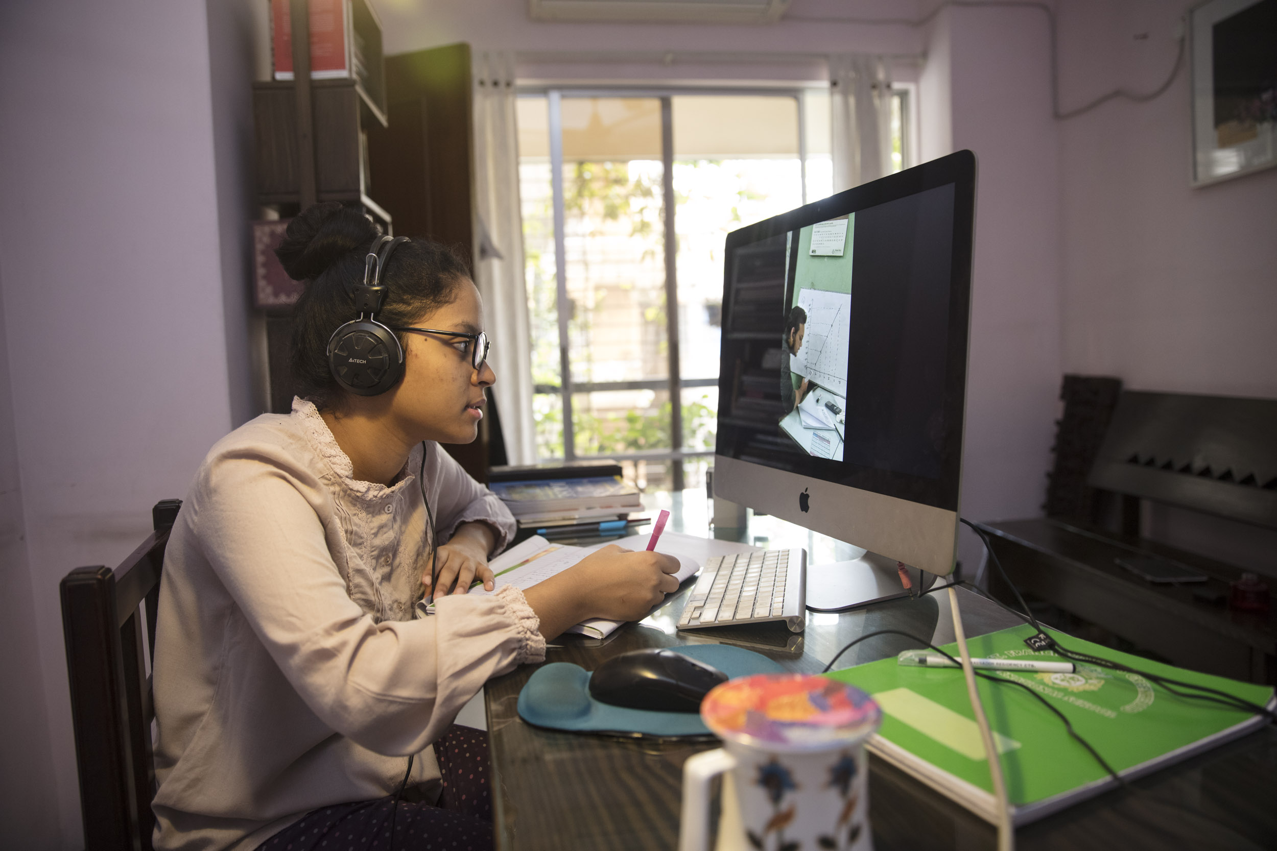 A young lady using her desktop and writing down notes in a notebook