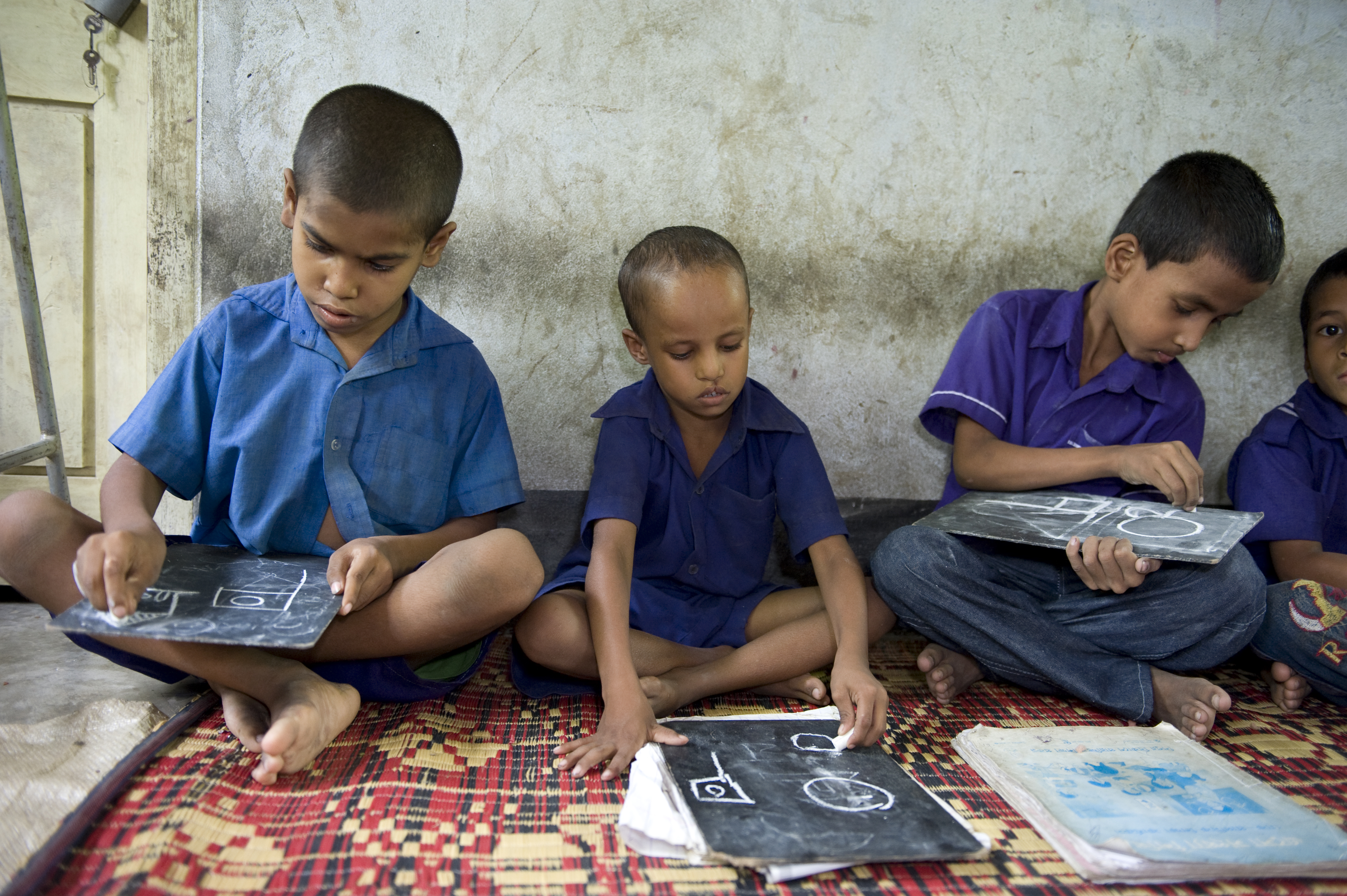 Left) Rashedul Uddin, 10, and his classmates are drawing on a chalkboard at Brahmankata Pre Primary School, Chakaria, Cox's Bazar, on 19 June 2011. Born with no impairments, between the ages of 4 and 5, Rashedul began to suffer paralysis throughout his body, affecting not only his movement but also his speech. He comes to school alone with the help of a crutches and loves to study.