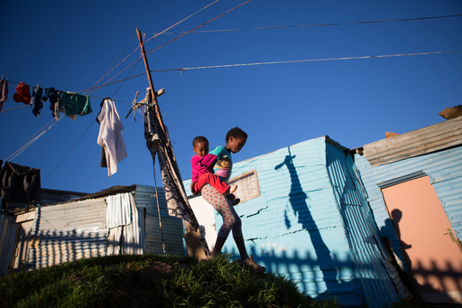 On 22 June 2016, a young girl and her baby sister hang up the washing in Imizamu Yethu Township, an informal settlement in Cape Town, South Africa where many young children are not attending school and families living there face extreme poverty