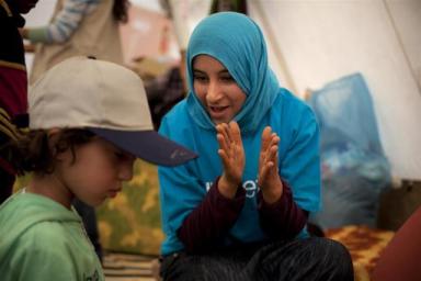 On 18 March, a UNICEF volunteer interacts with children at a UNICEF-supported child-friendly space in a transit camp on the Tunisian-Libyan border. The volunteer is wearing a T-shirt bearing the UNICEF logo. The camp hosts third-country nationals who had been living in Libya.