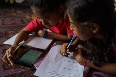 Phnom Penh (Cambodia). Nha Nha helps her smaller sister Sopheap with her home-works using a live streaming lesson.